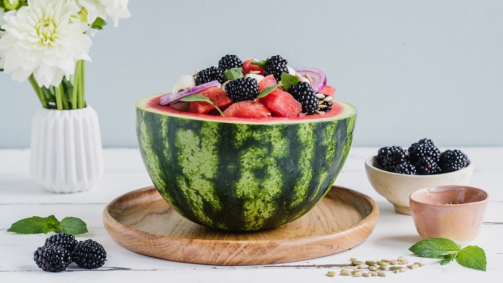 Sałatka podana w arbuzie z kulkami mozzarelli, czarnymi jeżynami, czerwoną cebulą i rukolą